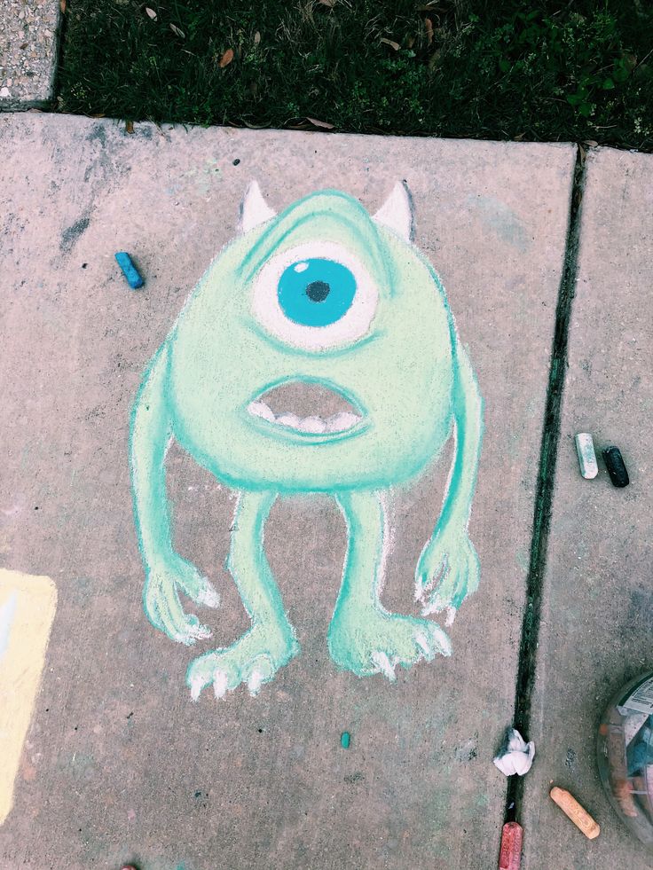 a drawing of an evil looking creature on the sidewalk next to some crayons