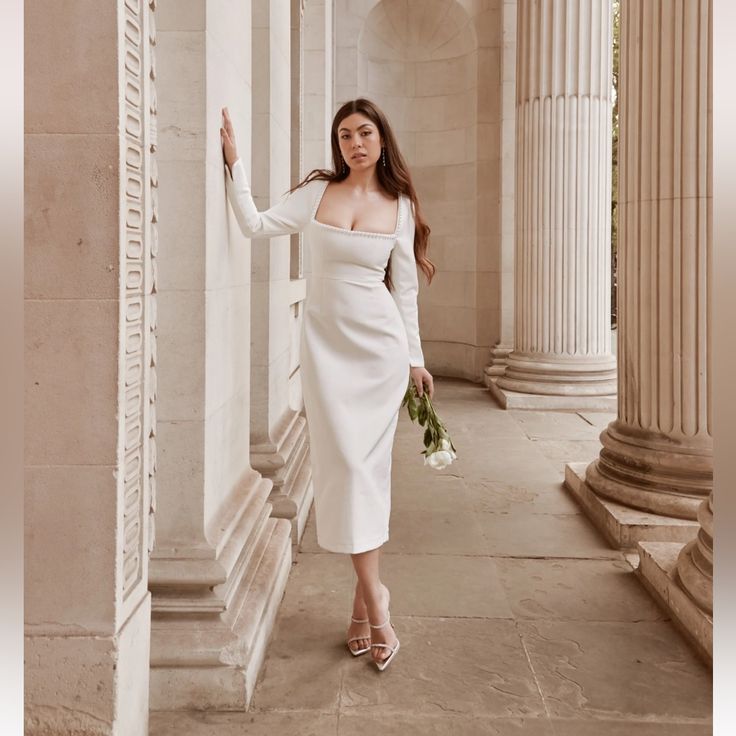 a woman in a white dress is standing by columns