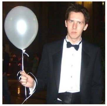 a man in a tuxedo holding a white balloon with a black bow tie