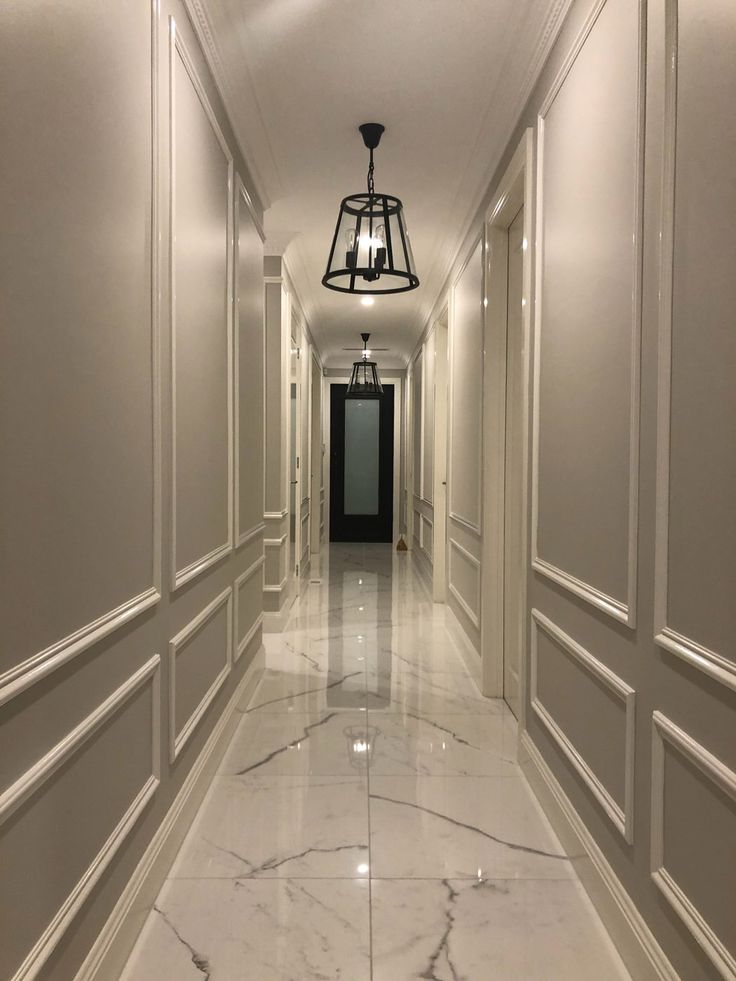 a long hallway with white walls and marble flooring is lit by a light fixture