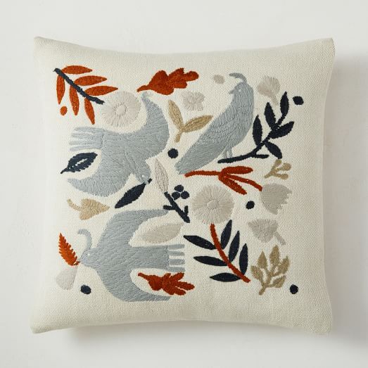 an embroidered pillow with birds and leaves on it