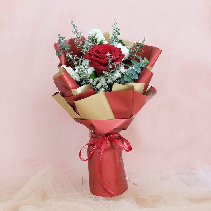 a bouquet of flowers wrapped in red and gold paper on a pink background with the word love written below it