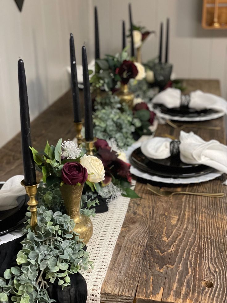 the table is set with black and white plates, silverware, flowers and greenery