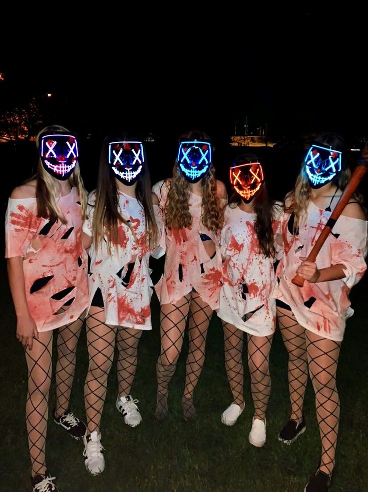 five girls in costumes with masks on their faces and holding baseball bats at night time