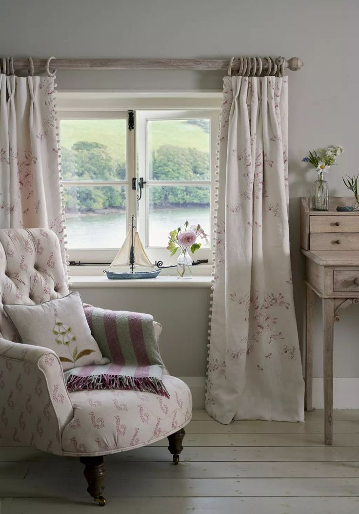 a chair sitting in front of a window next to a table with flowers on it