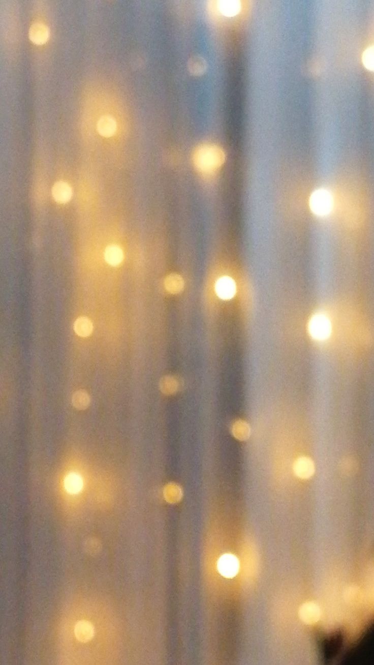 a blurry image of some lights on a window with curtains in the foreground