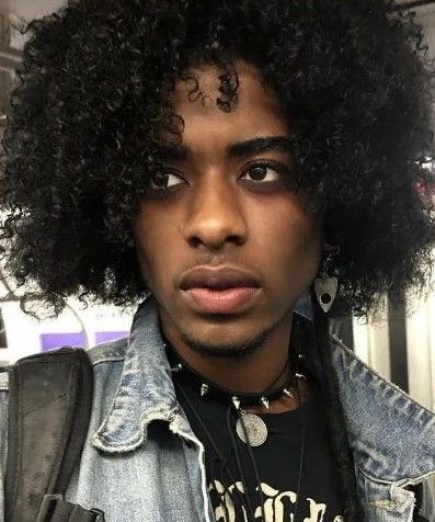 a young man with curly hair and piercings on his forehead wearing a denim jacket