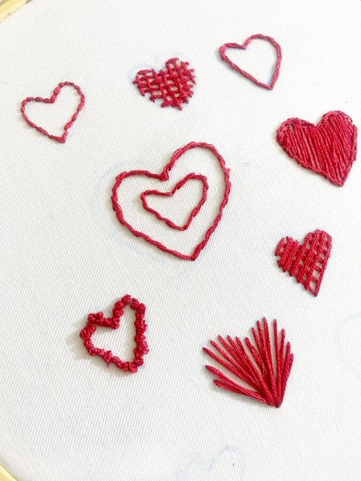 some red hearts are on a white table cloth and the thread is stitched together