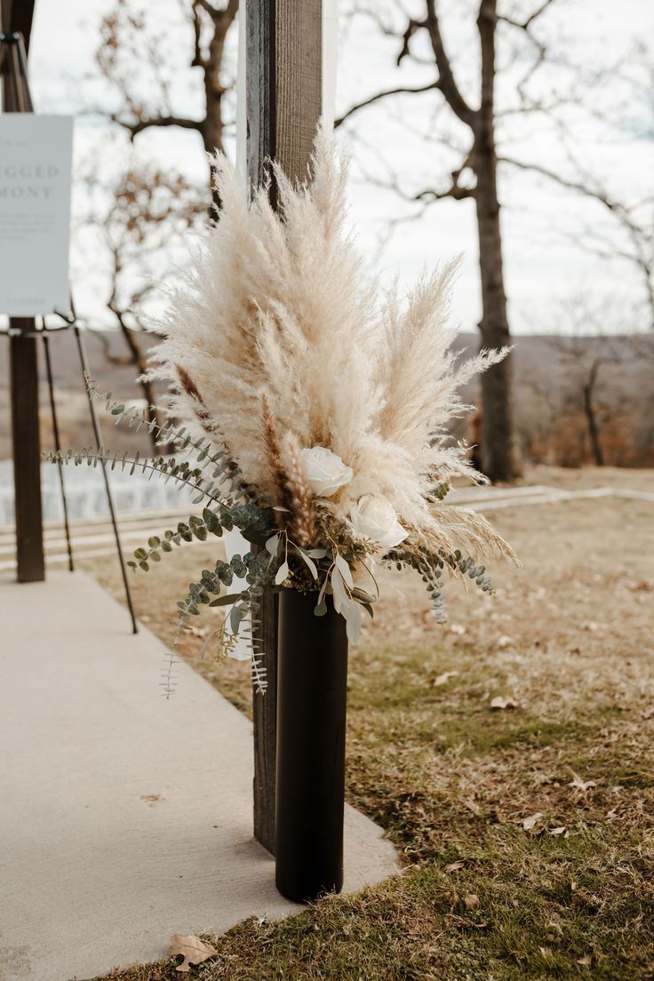 a tall vase filled with white flowers sitting on the side of a road next to a street sign