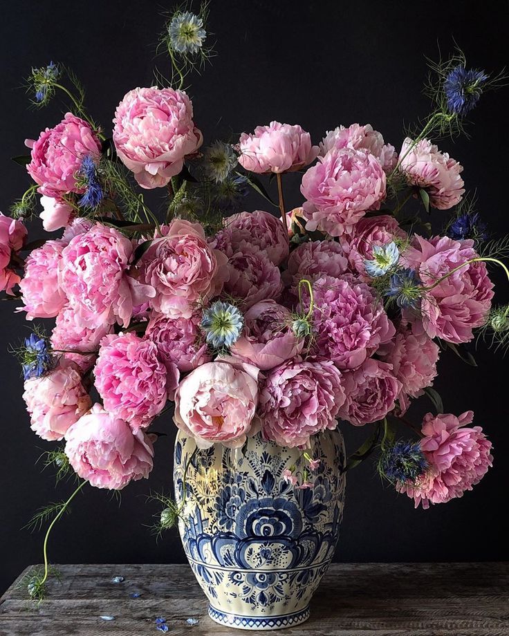 a blue and white vase filled with pink flowers on top of a wooden table next to a black wall