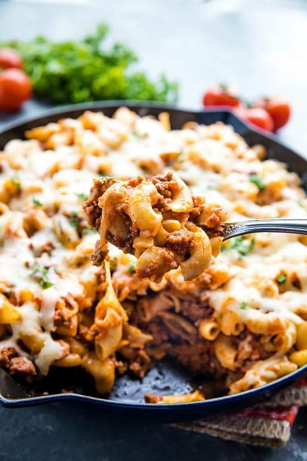 a close up of a fork in a casserole dish with meat and cheese