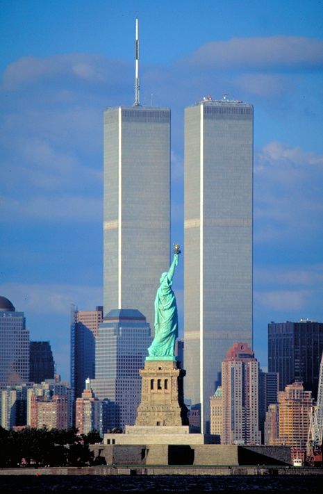 the statue of liberty stands in front of two tall skyscrapers that rise into the sky