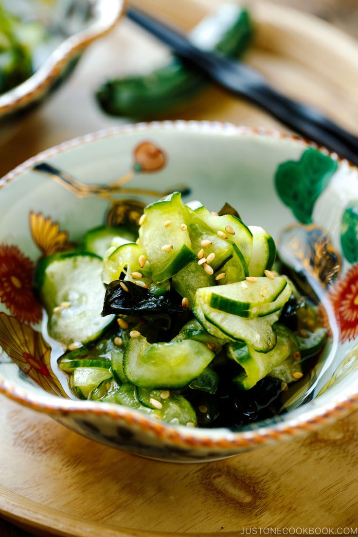 a bowl filled with cucumbers and other vegetables on top of a wooden table