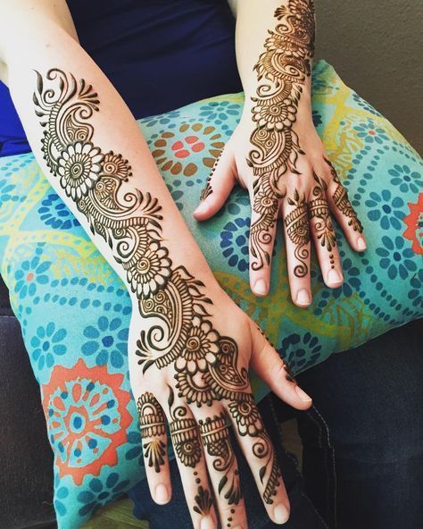 a woman's hands with henna tattoos on her arm and hand, sitting in a chair