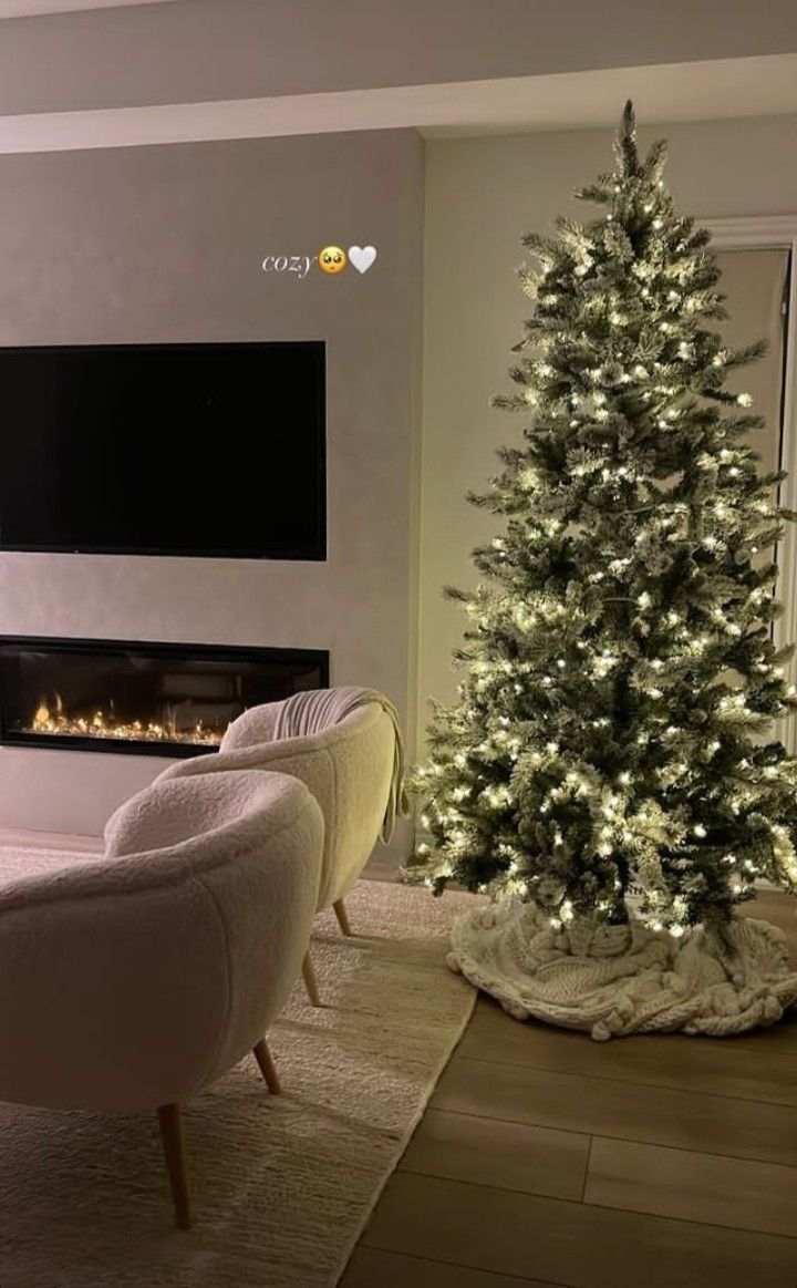 a living room with a christmas tree and two chairs in front of the fire place