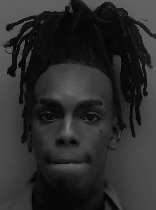 a black and white photo of a man with dreadlocks on his head looking at the camera