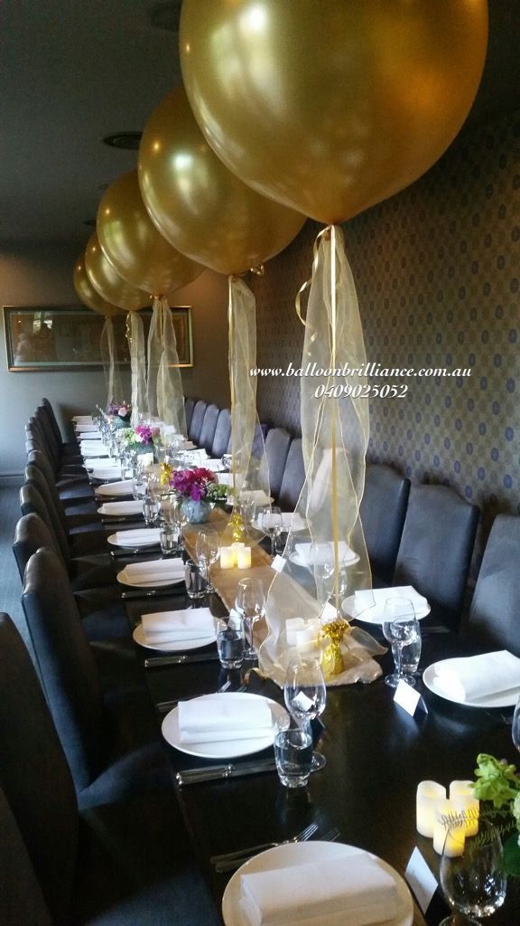 a long table is set with plates, silverware and gold balloons in the background