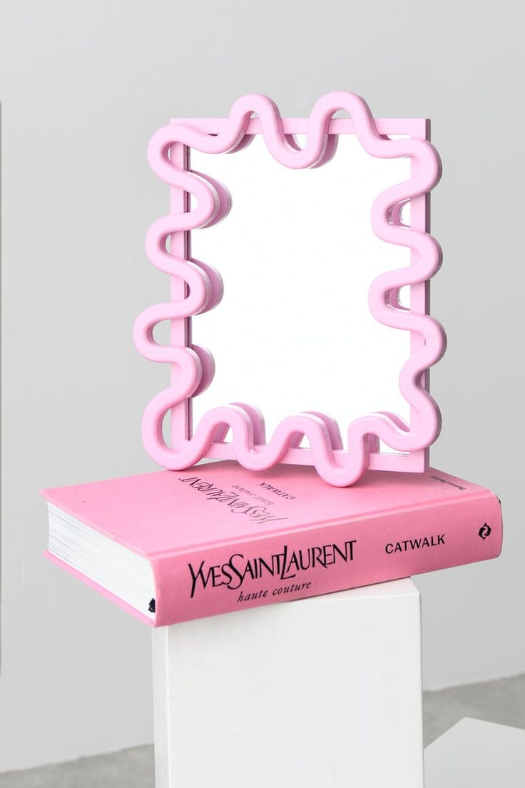 a pink mirror sitting on top of a stack of books in front of a white wall