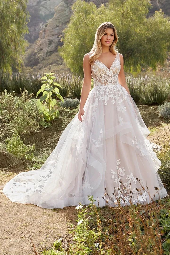 a woman in a wedding dress standing on a dirt path with bushes and trees behind her