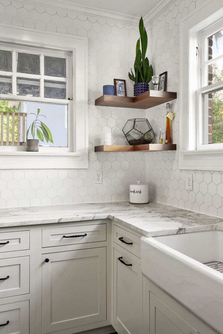 a kitchen with white cabinetry and marble counter tops, along with open shelving above the sink