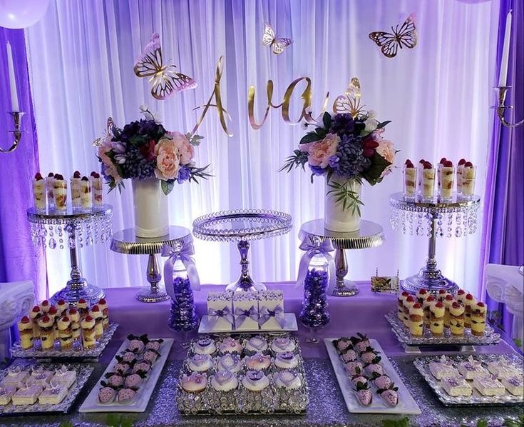 a table topped with lots of cakes and cupcakes next to tall vases filled with flowers