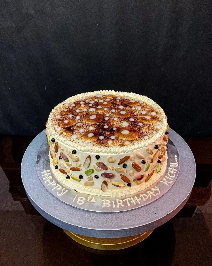 a birthday cake with nuts and frosting on a table in front of a black backdrop