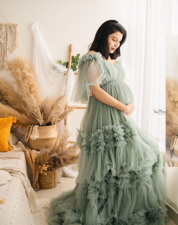 a pregnant woman in a green dress standing next to a bed