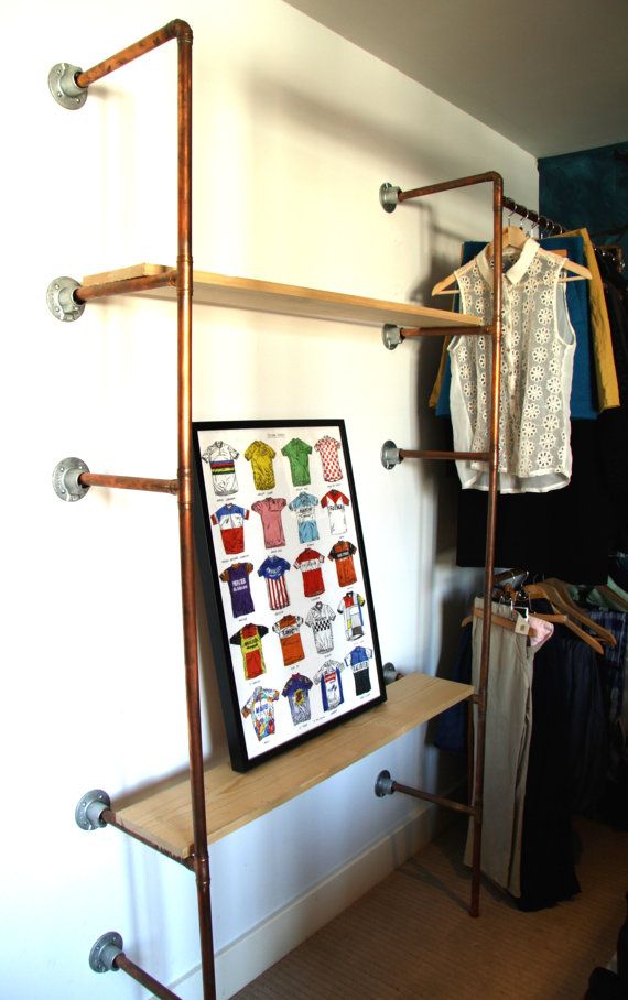 a clothing rack with clothes hanging on it next to a white wall and wooden shelves