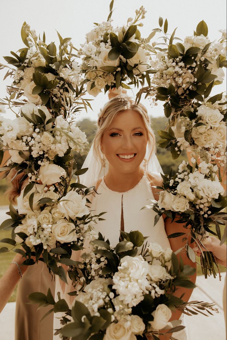 a woman standing in front of a flower arch with flowers and greenery around her