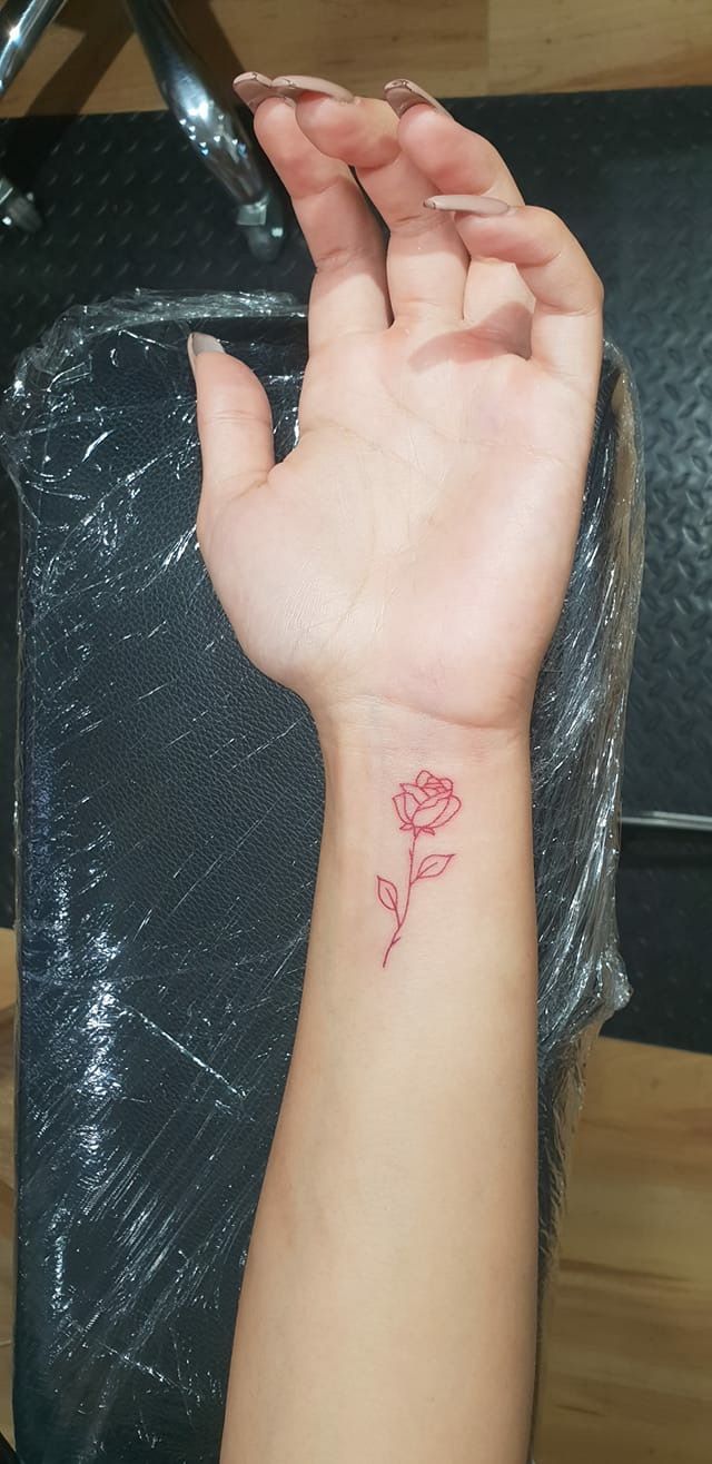 a woman's hand with a small red rose tattoo on her left arm and wrist