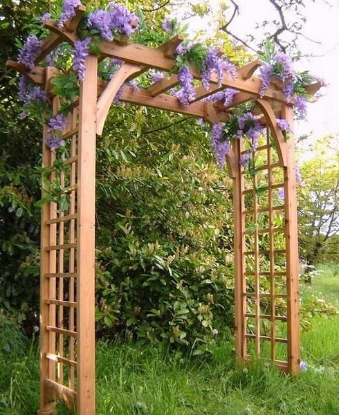 an outdoor wooden arbor with purple flowers growing on it's sides and green grass in the background