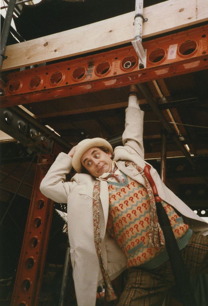 a man in a suit and tie standing on top of a wooden structure with his hands behind his head