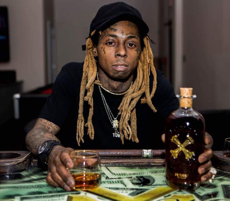 a man with dreadlocks sitting at a table next to a bottle of whiskey