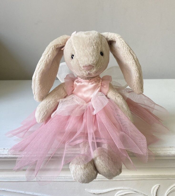 a stuffed rabbit wearing a pink dress sitting on top of a table