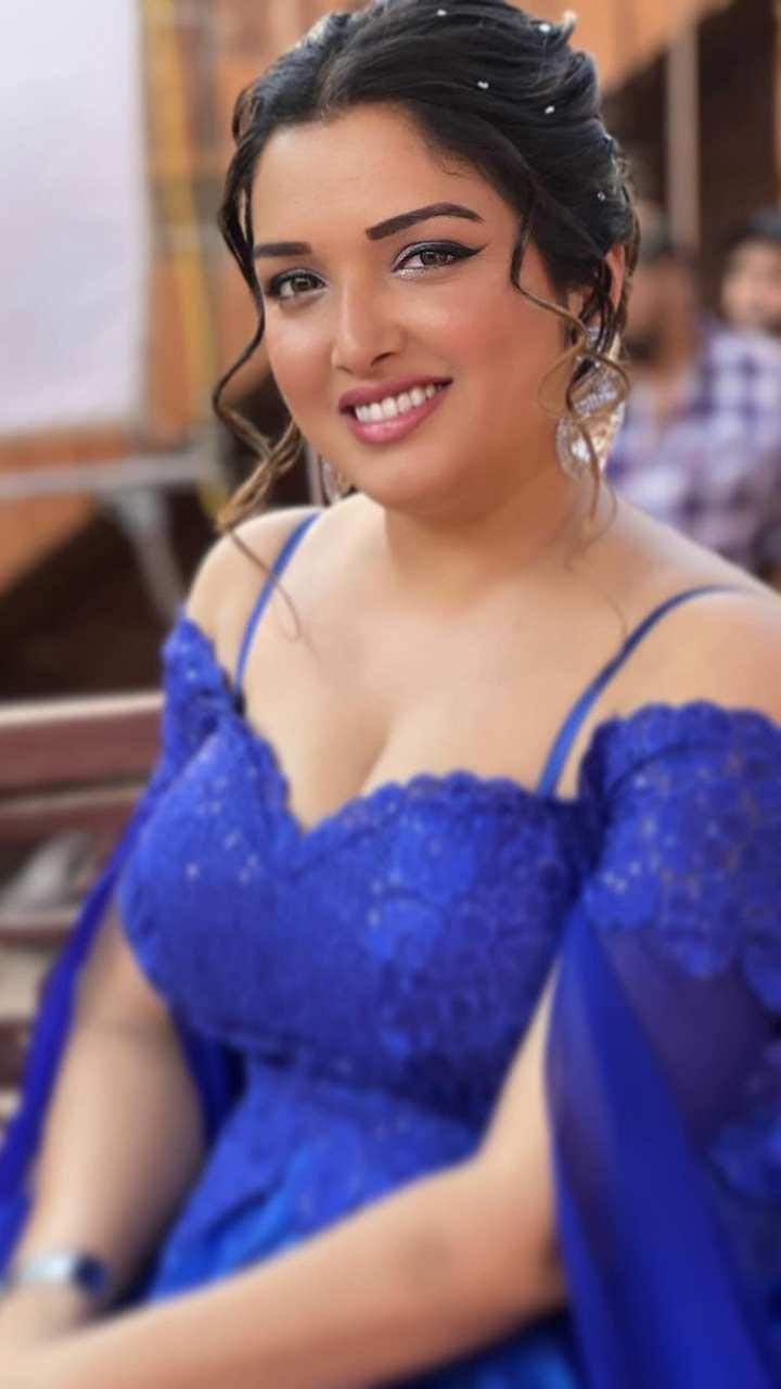 a woman in a blue dress sitting on a bench smiling at the camera with people behind her