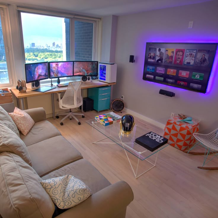 a living room filled with furniture and two computer monitors on top of a wall mounted flat screen tv