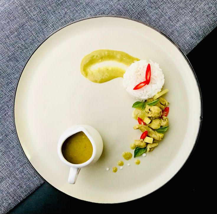 a white plate topped with food next to a cup of green liquid and sauce on top of it