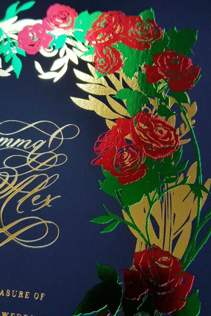 the wedding card is decorated with flowers and gold foil lettering on it's blue background