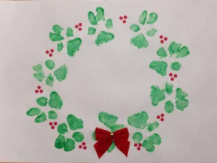 a paper wreath made with green and red handprints that have been placed in the shape of a bow