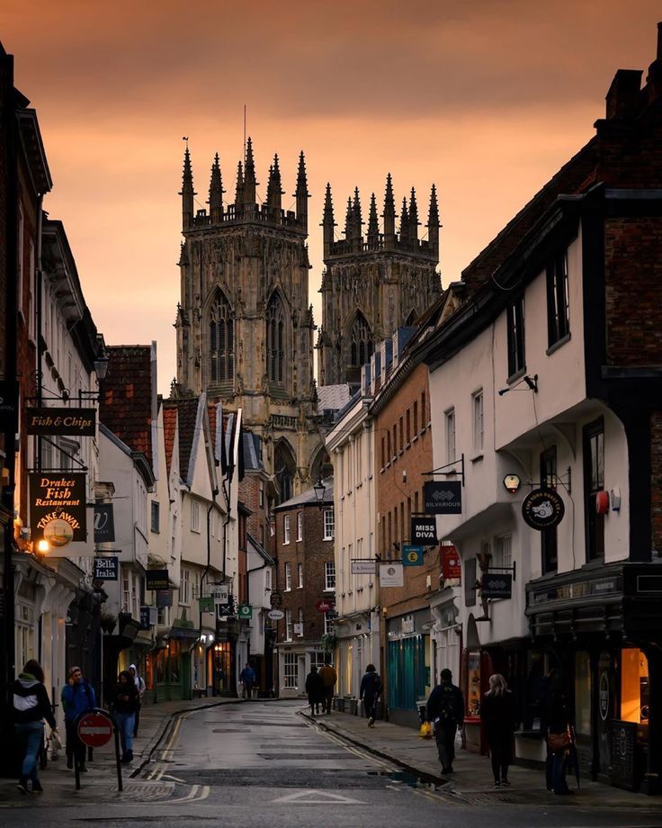 people are walking down the street in front of some buildings and an old church tower