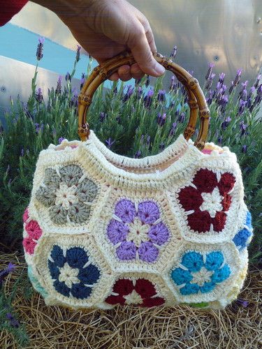 a hand holding a crocheted purse in front of some purple and white flowers