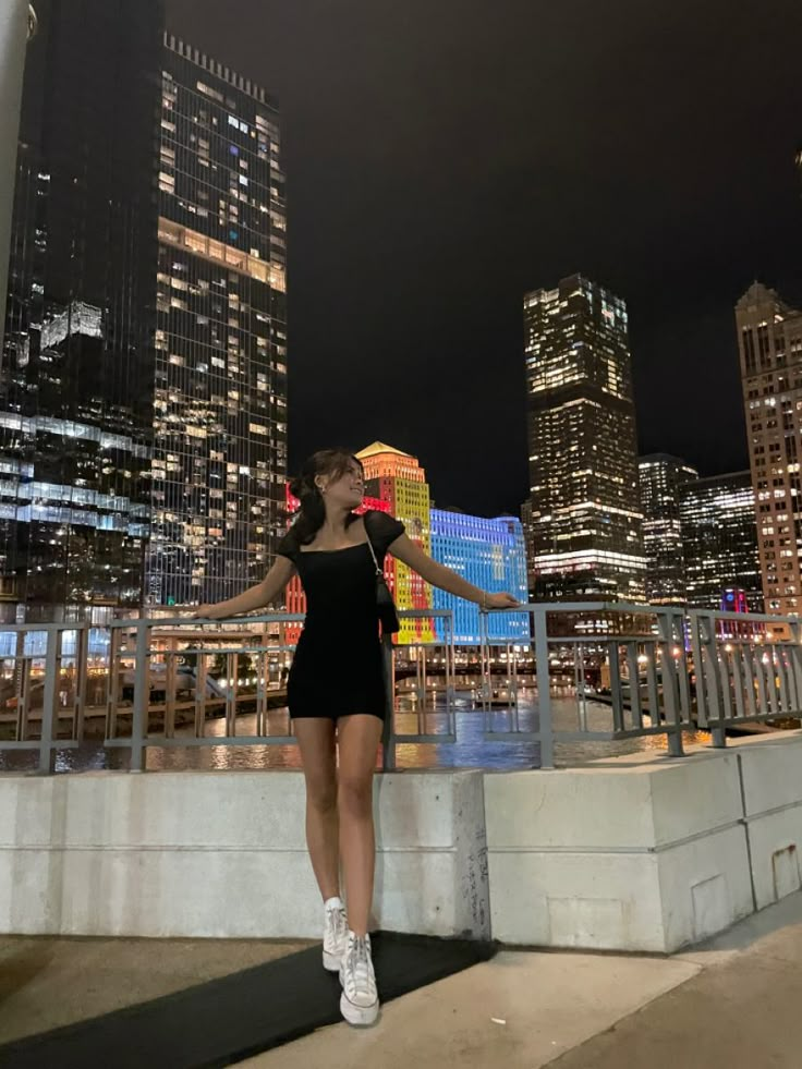 a woman is standing on a ledge in front of some tall buildings at night time