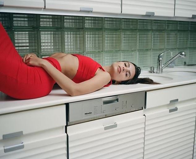 a woman laying on top of a kitchen counter next to a dishwasher and sink