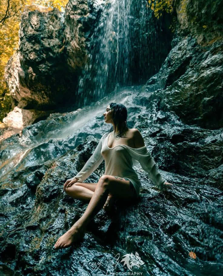 a woman is sitting on the rocks in front of a waterfall with her eyes closed