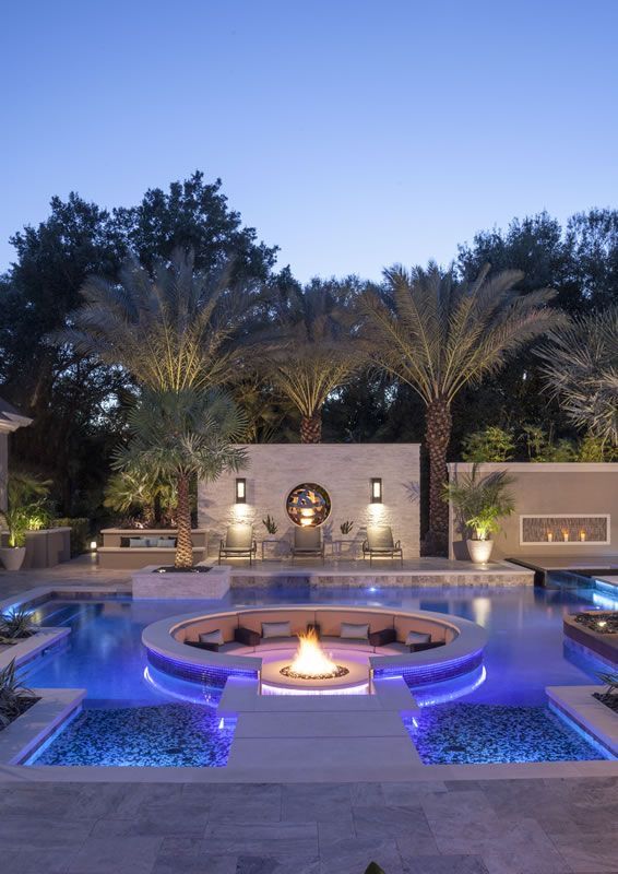 an outdoor fire pit surrounded by palm trees and landscaping at night with lights on it