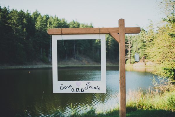 a wooden cross with a photo frame hanging from it's side in front of a lake