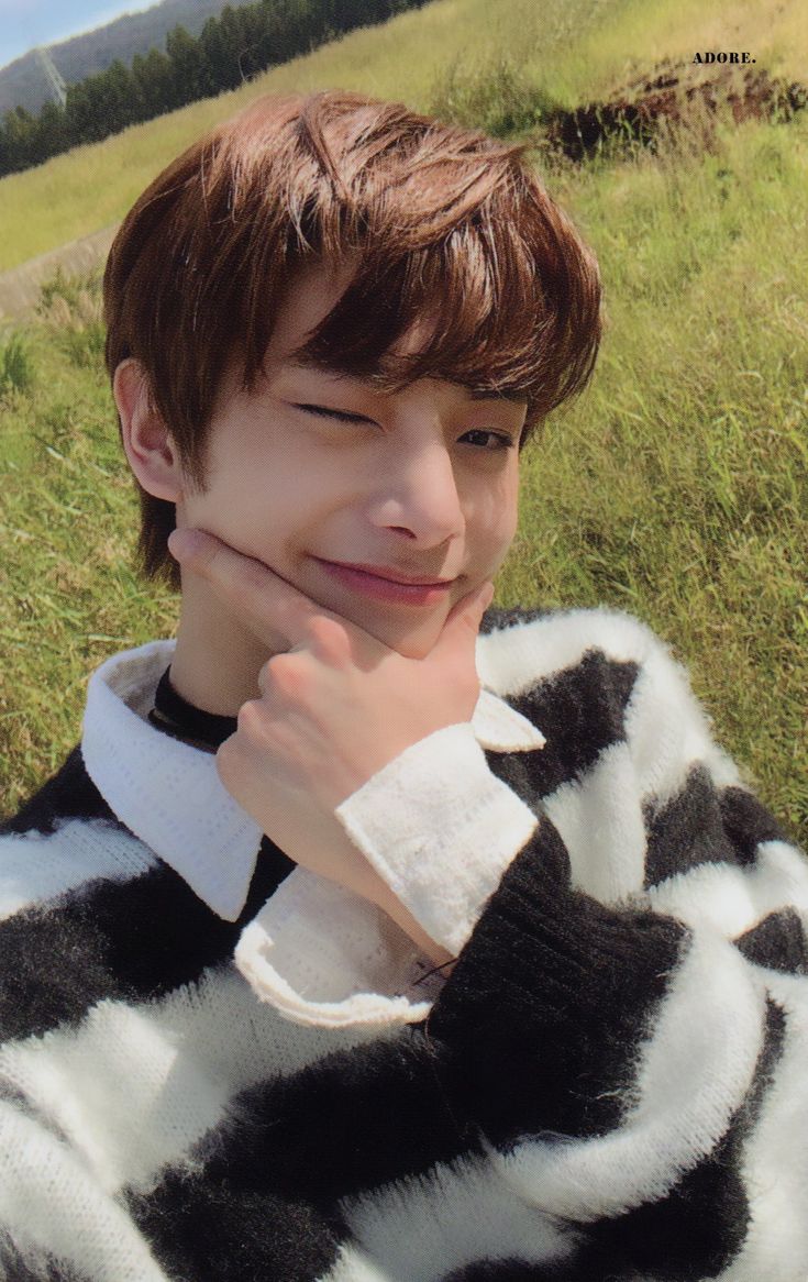 a young man sitting on top of a lush green field next to a hillside covered in grass