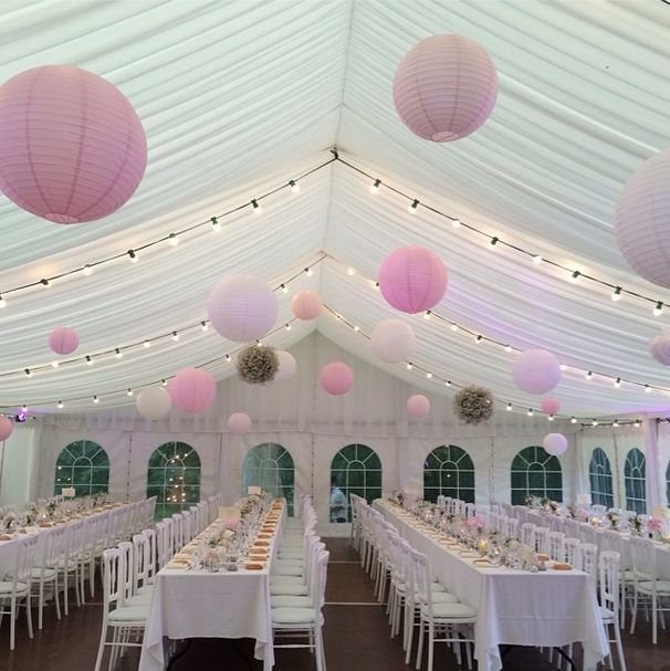 the inside of a tent with tables, chairs and paper lanterns hanging from the ceiling