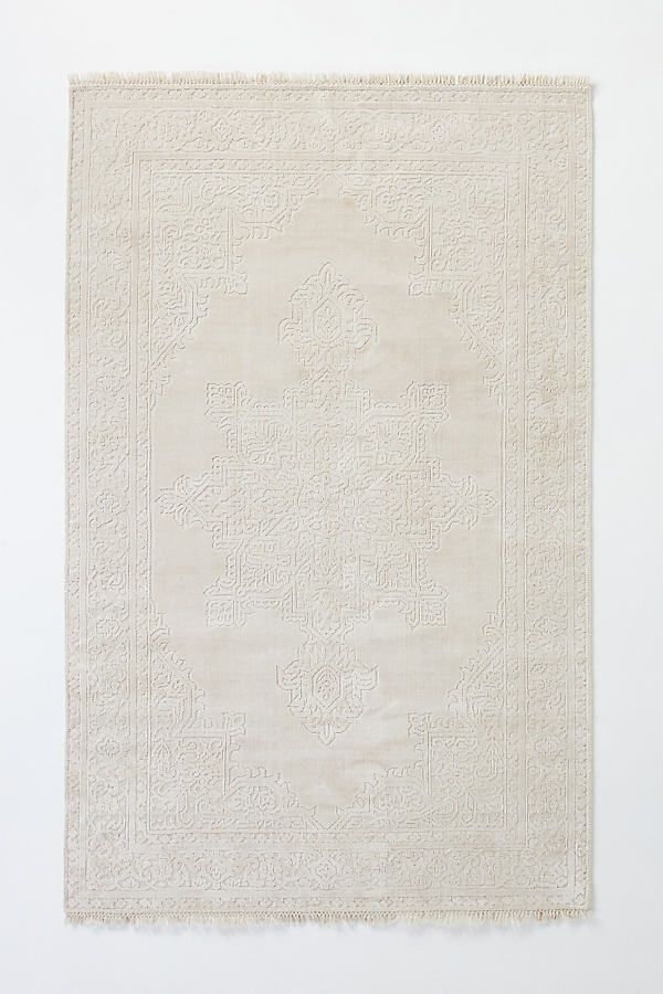 a white rug with an intricate design on the front and back side, against a white wall