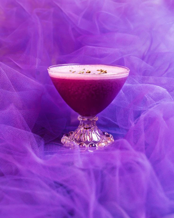 a drink in a goblet sitting on a table with purple tulle around it